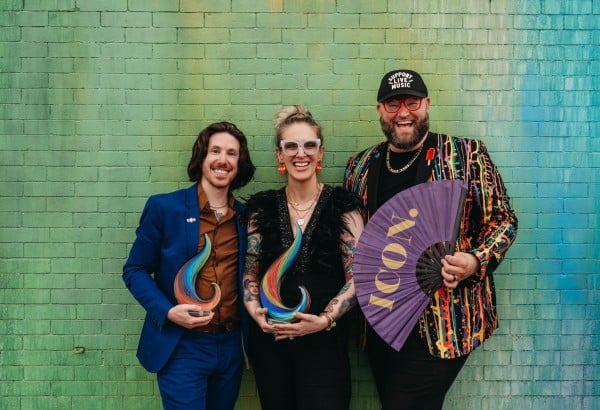 Three people standing and smiling with a background of a green wall.