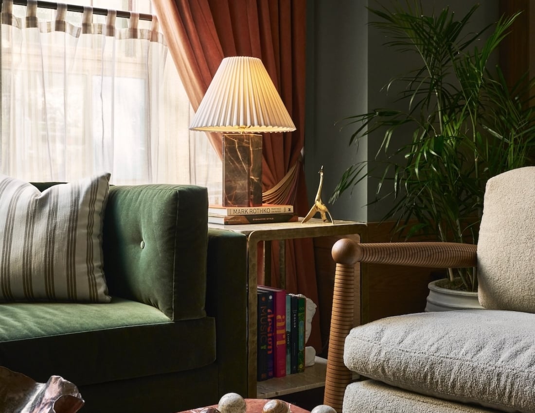 A plush green velvet sofa anchors a richly decorated living space. A pleated lamp and red marble coffee table with decorative balls are near rust-colored window curtains. MARK ROTHKO, CREATIVE STYLE, MUSIC, design, ART, COLOR.