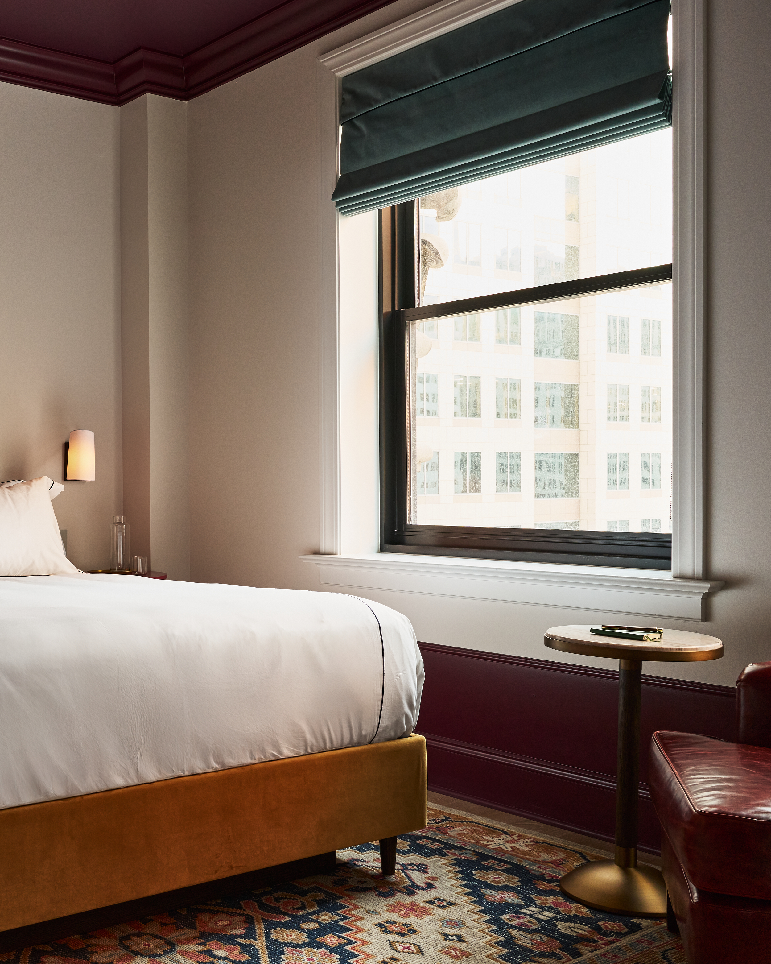 A hotel room with a bed, a window showing a city view, and a small table.