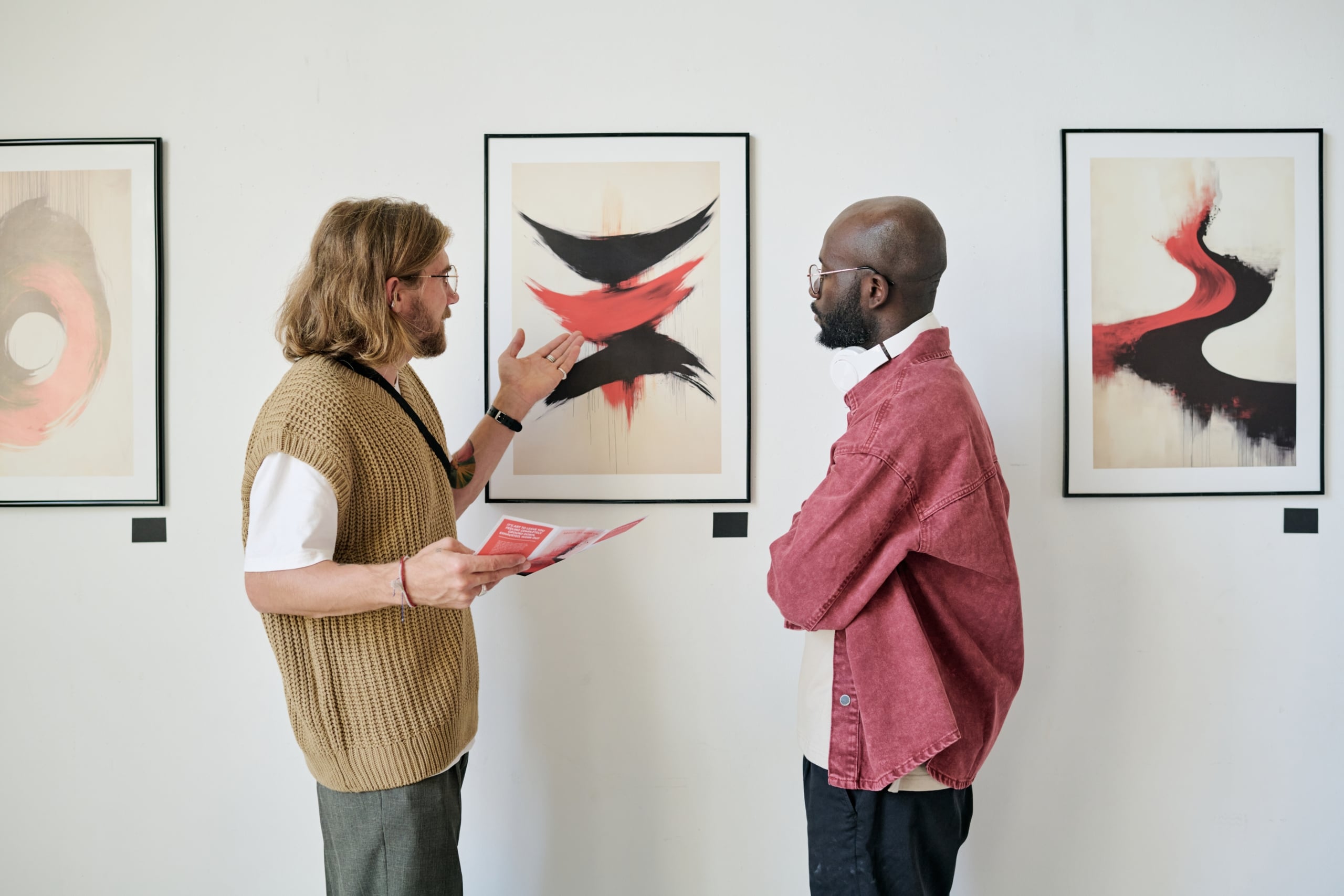 Two men in an art gallery. One, holding a leaflet, gestures at an abstract painting as the other listens. Leaflet text: "IT'S A SIGN TO LEAVE YOU FEELING DRAINED, EXHAUSTED, WORN OUT?"