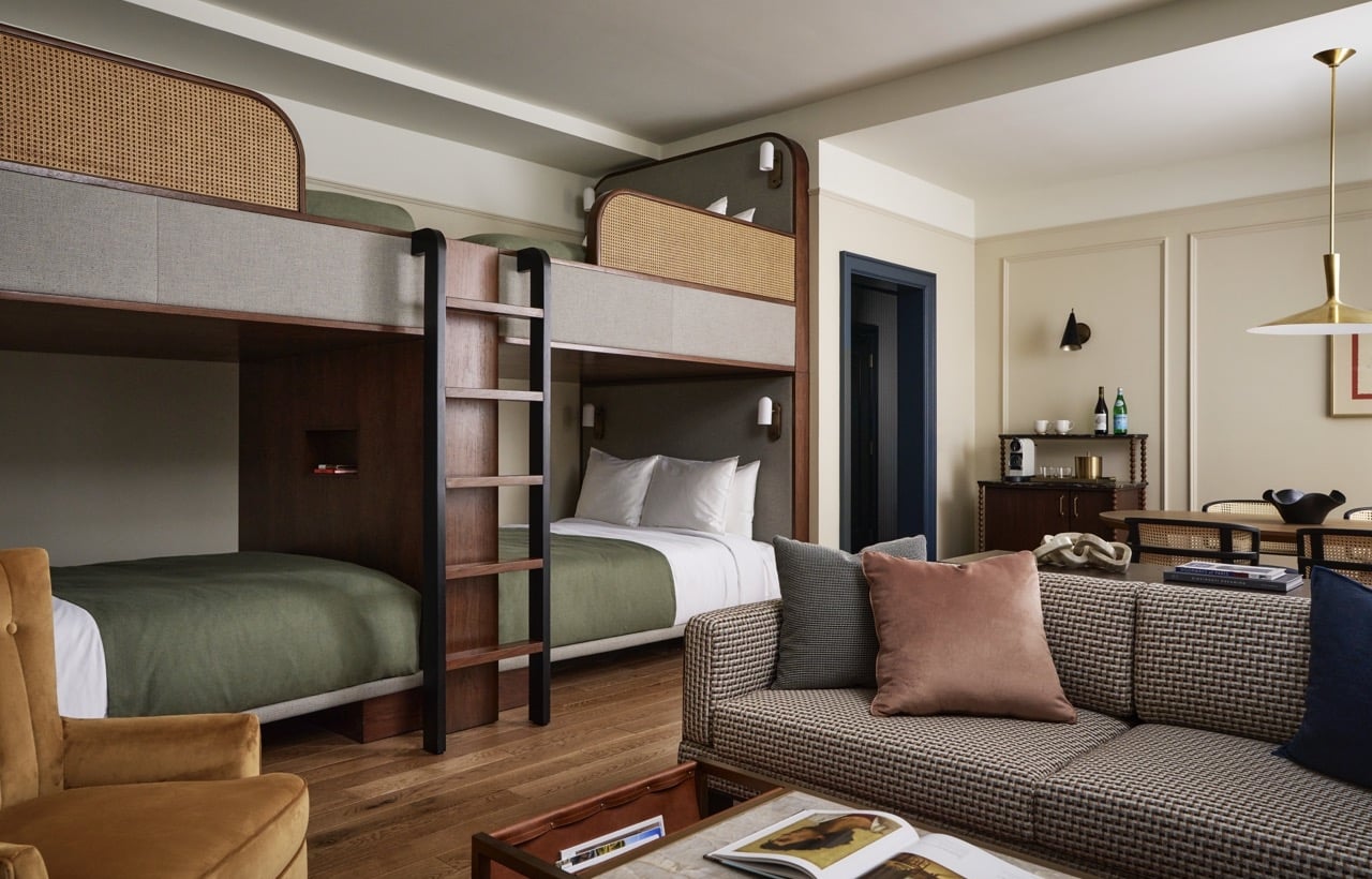 Modern dark wood bunk beds with green bedding and cane accents feature in a stylish room, alongside a patterned sofa, coffee table, and mini-bar, all on hardwood floors.
