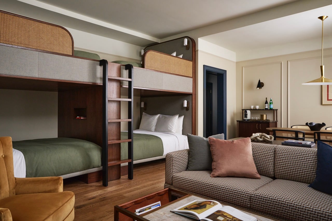 Modern dark wood bunk beds with green bedding and cane accents feature in a stylish room, alongside a patterned sofa, coffee table, and mini-bar, all on hardwood floors.
