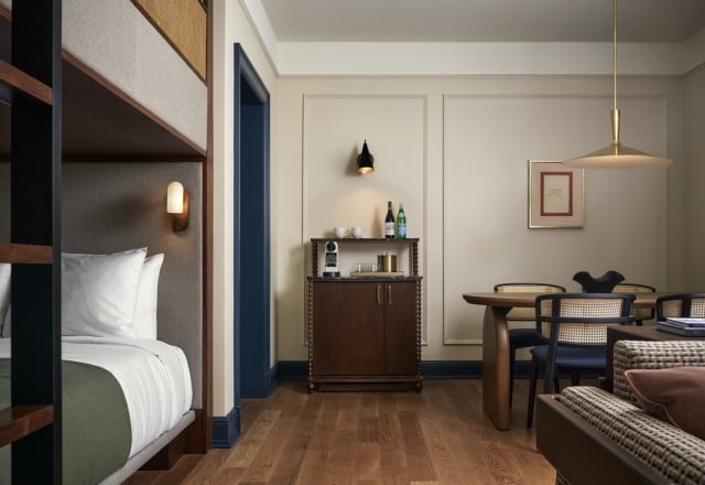 Bunk bed, minibar cabinet, and dining table with cane chairs furnish a room. Hardwood floors, light walls, dark blue trim. Text: DOORWAYS.