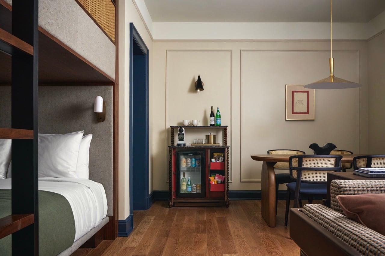 A room features a lower bunk, a minibar with fridge/coffee maker, and a dining table. Light walls, wooden floors define the space, with "DOORWAYS" on a couch.