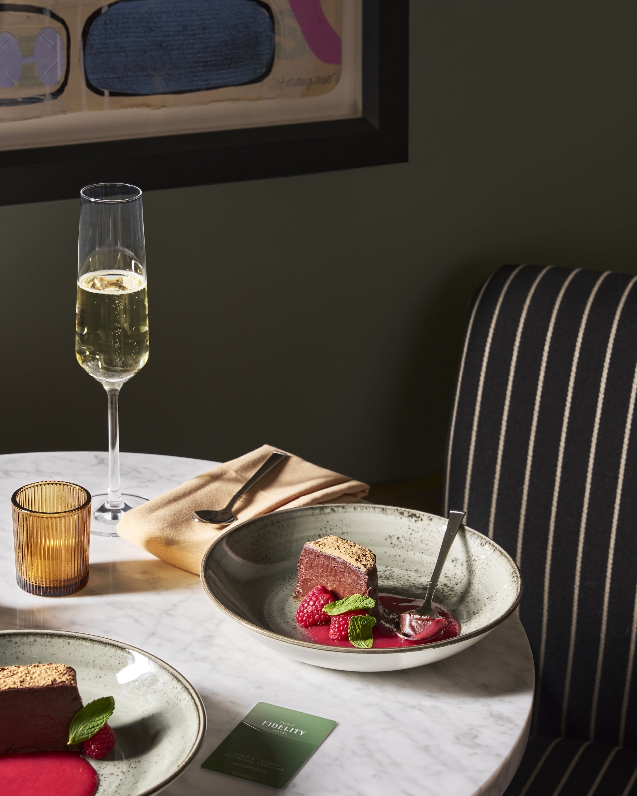 Chocolate desserts with raspberries and mint are served on a marble table with a champagne flute and candle in a restaurant.
