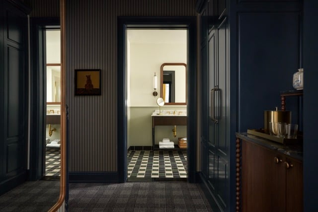 A dark-trimmed hallway opens to a bathroom with a black-and-white checkered floor and vanity. Striped walls, a plaid carpet, and a fox painting adorn the hallway.