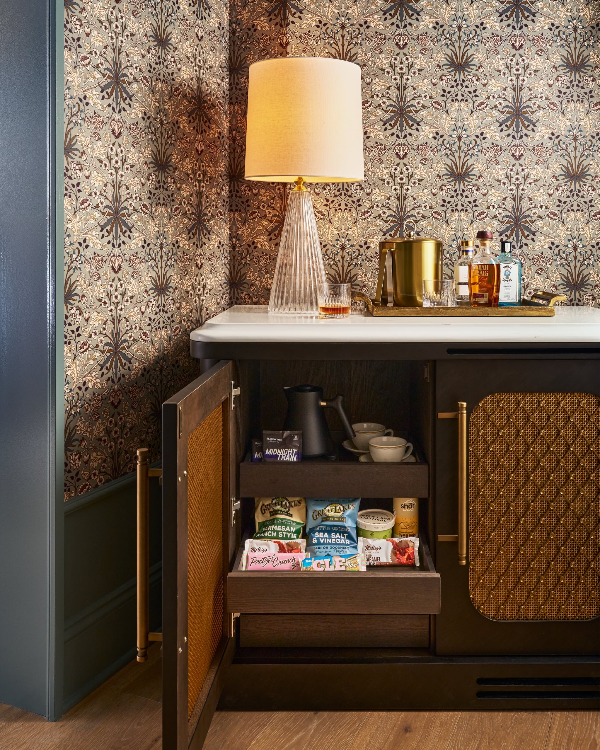 A dark wooden minibar cabinet, with an open door, reveals a kettle and snacks.