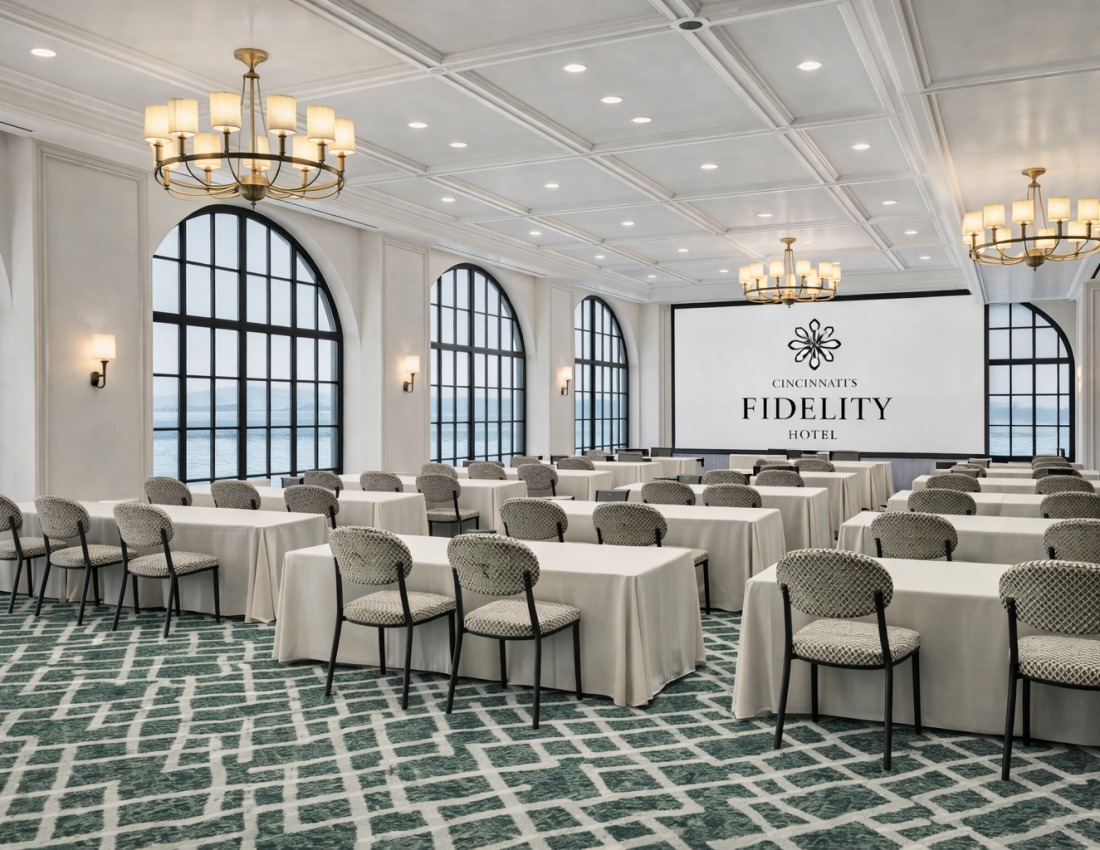 A large conference room displays rows of tables and patterned chairs facing a screen with:
CINCINNATI'S
FIDELITY
HOTEL
Arched windows overlook water, with chandeliers illuminating the space.