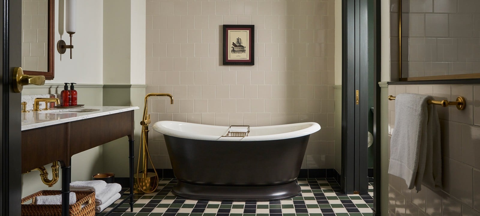 A dark freestanding bathtub sits centrally in a bathroom featuring a vanity with **FIRE** brand soaps, brass fixtures, and a black, white, and green checkerboard tiled floor.