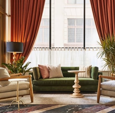 A green velvet sofa and two beige armchairs furnish a lounge area, placed before large windows with orange curtains and sheer drapes.  **Text:**
shape out minds. (v.) to get souls out of the mess. (n.) a shape for souls to get out of the mess. shape out minds. (v.) to get souls out of the mess. (n.) a shape
