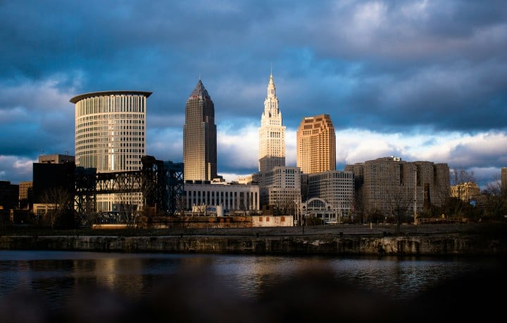Cleveland skyline reflected in the Cuyahoga River under dramatic storm clouds, with Terminal Tower lit by sunlight.