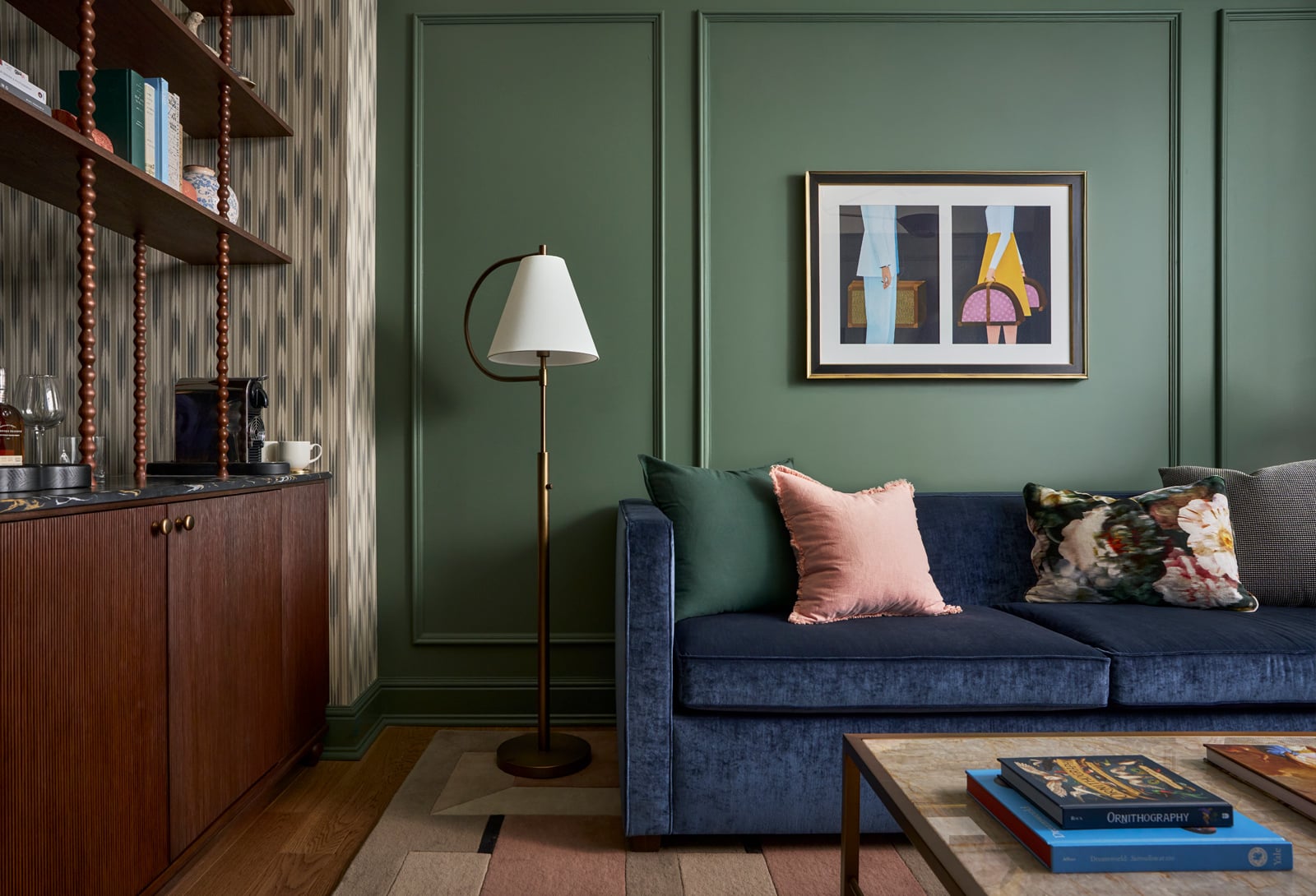A blue velvet sofa sits beside a brass floor lamp and a wooden bar cabinet in a room with dark green paneled and patterned walls. Text: GEOPHILUS, ORNITHOGRAPHY, Dronnable, Scandinavia, Yale.
