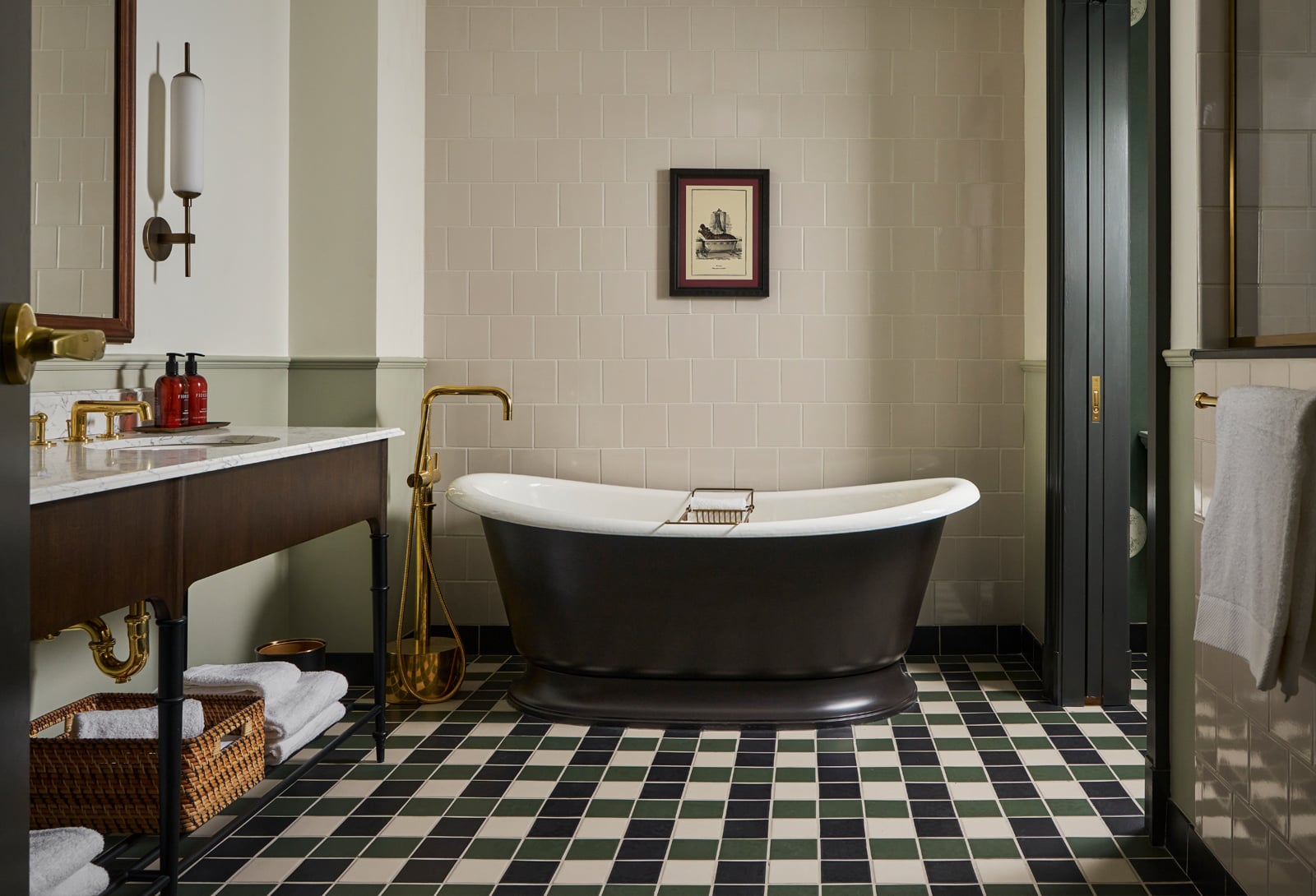 A freestanding dark bathtub sits prominently on a checkered floor in a sophisticated bathroom. Two bottles labeled 'FIRE FI' rest on the nearby vanity.