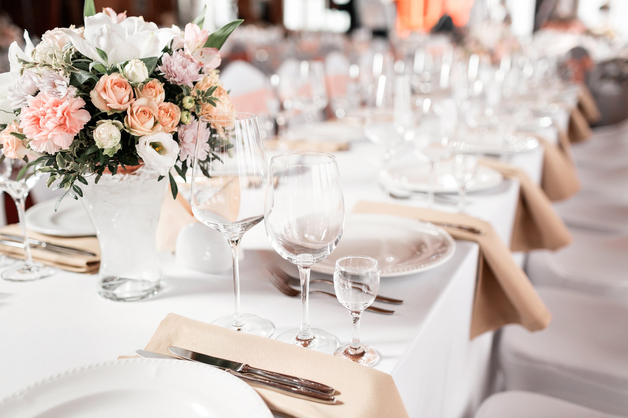 A vibrant floral centerpiece adorns a formal dining table, surrounded by wine glasses, plates, and cutlery on a white tablecloth, set for an event.