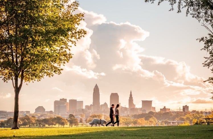 A joyful couple walking their dog in Cleveland, surrounded by beautiful scenery