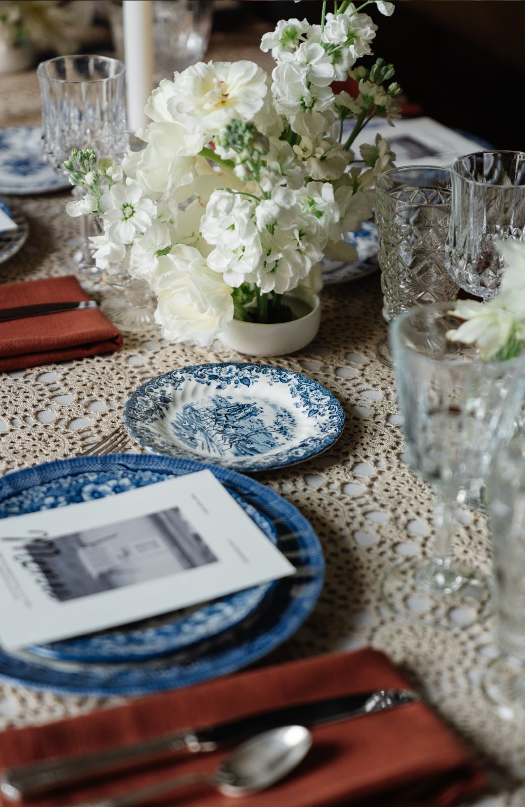 A table set for dining with blue and white plates, red napkins, and white flowers in a vase.