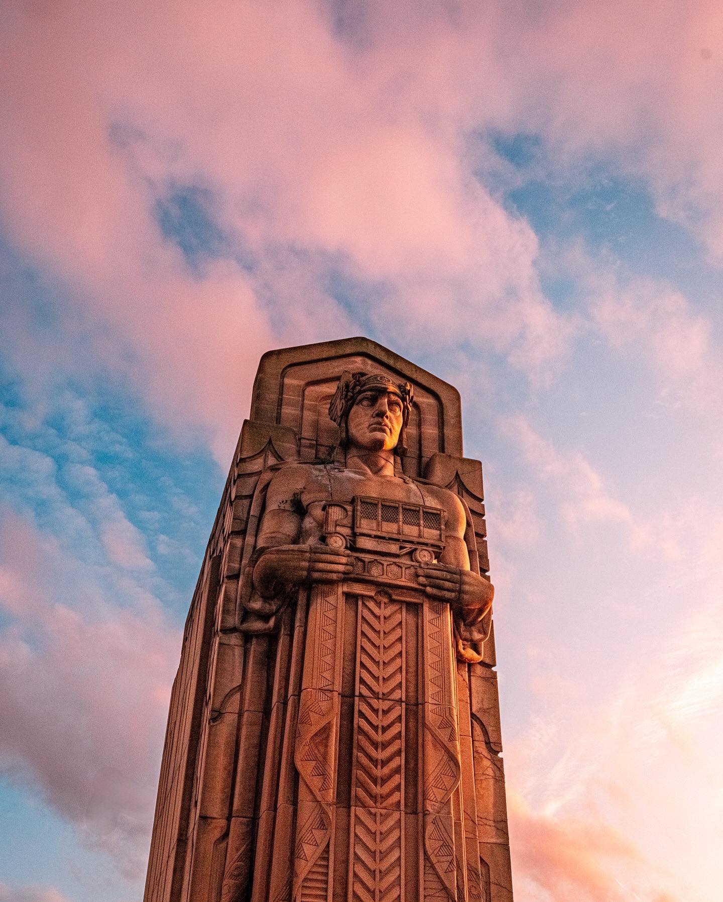 a statue of a man in a robe against a blue sky with pink clouds