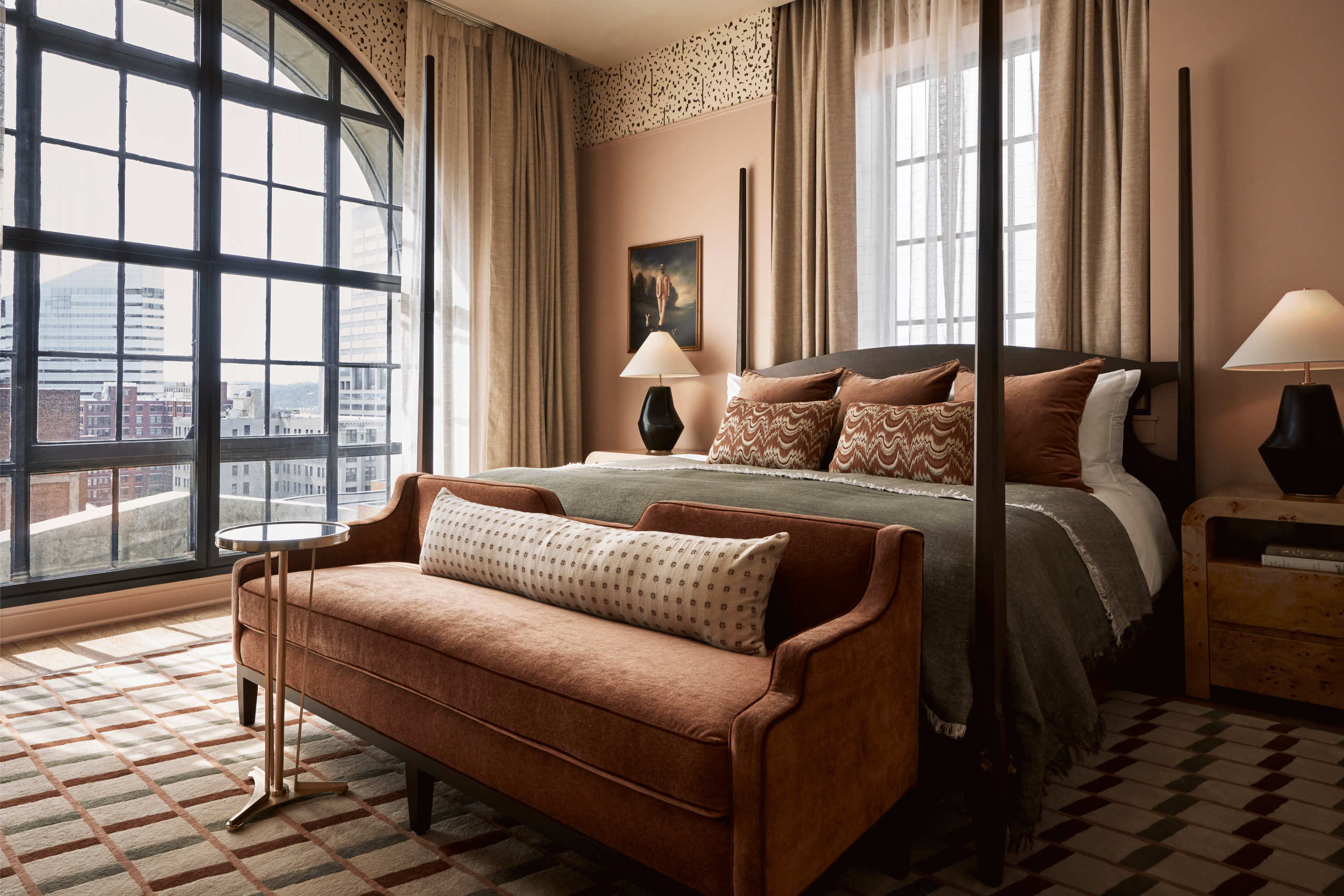 king size bed in hotel suite with night stands on both side and large arched window overlooking city