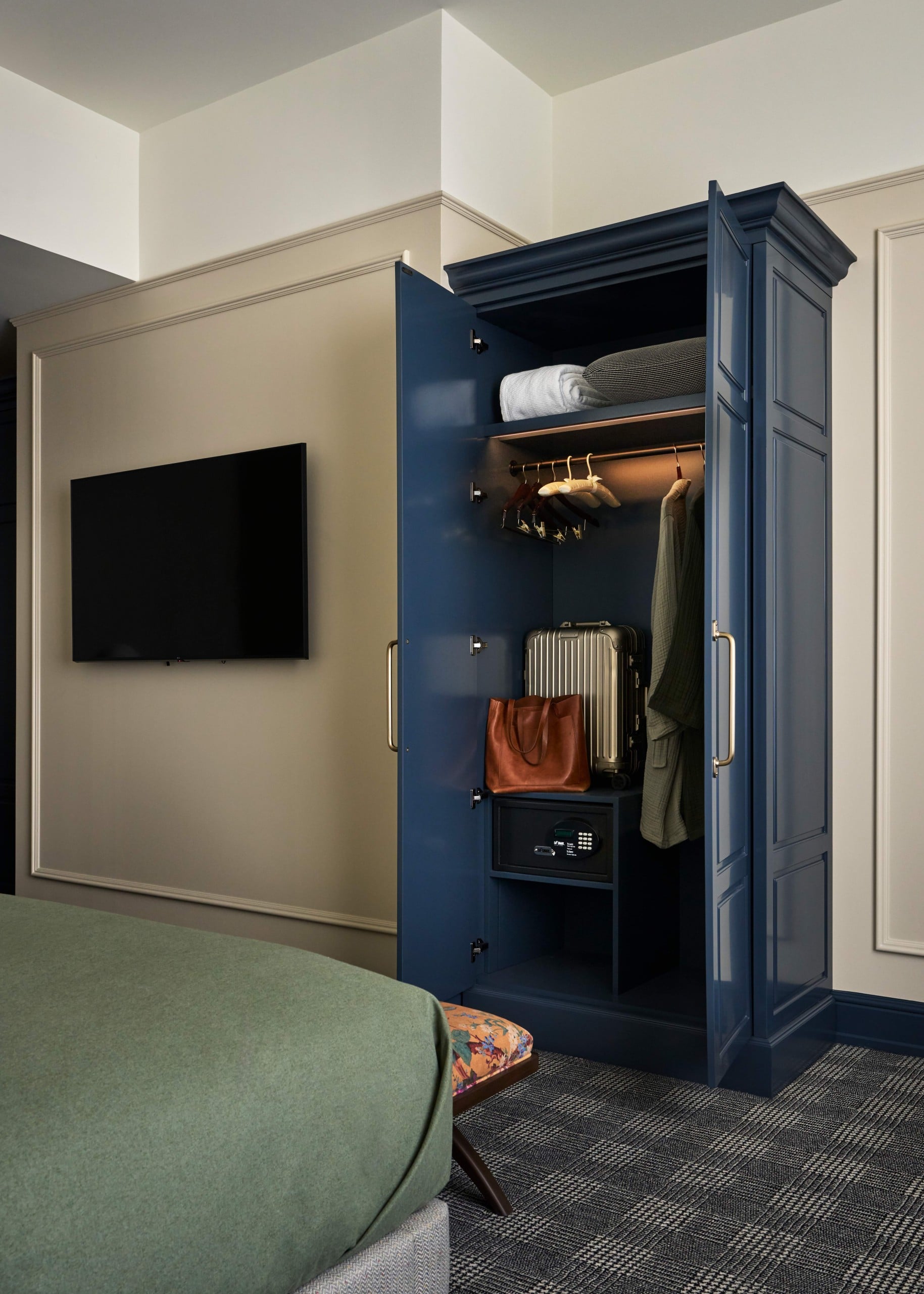 Blue Closet on right side of photo filled with luggage and a jacket hanging. Left side of photo features TV hanging on wall.