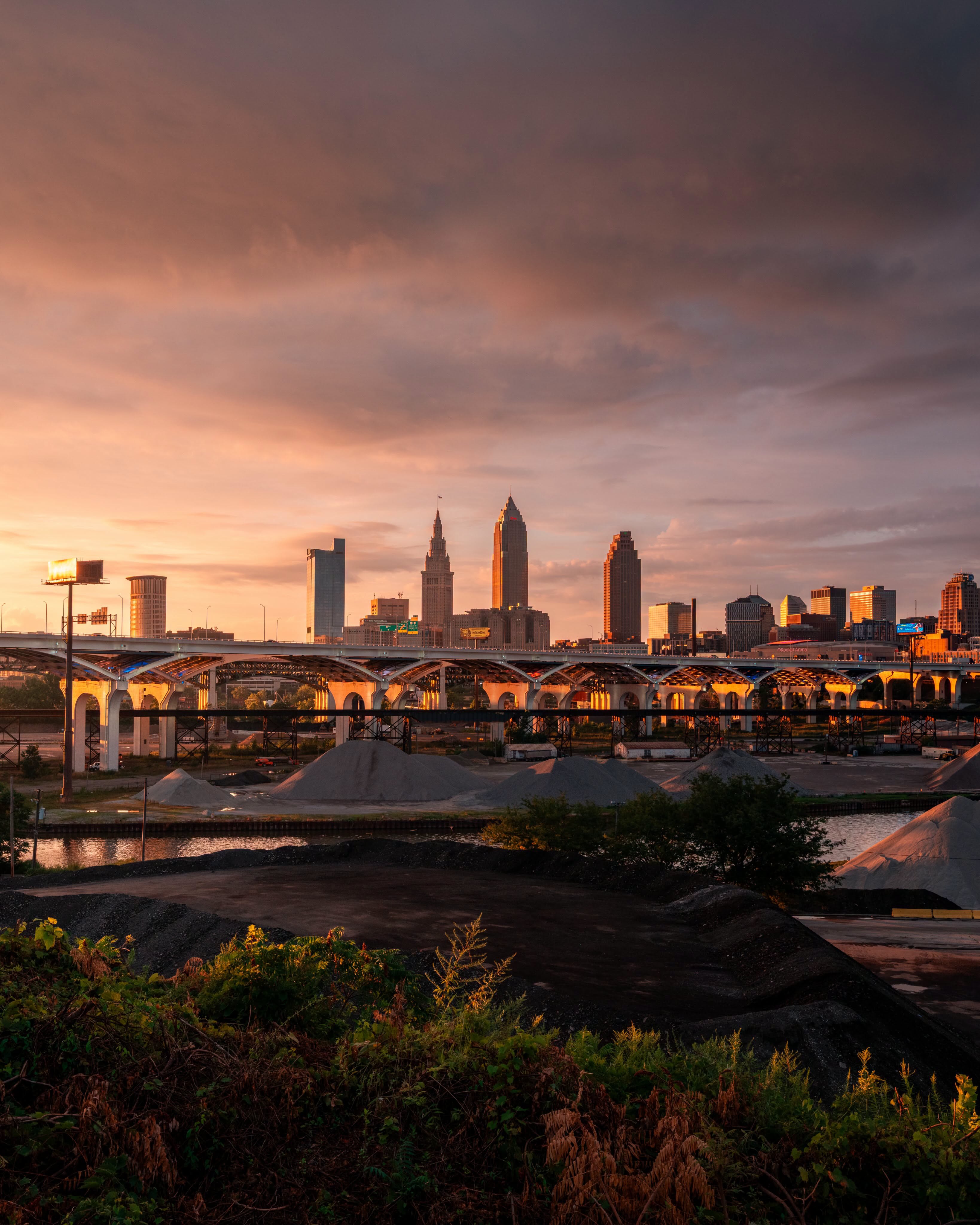 A city skyline at sunset with a bridge over a river