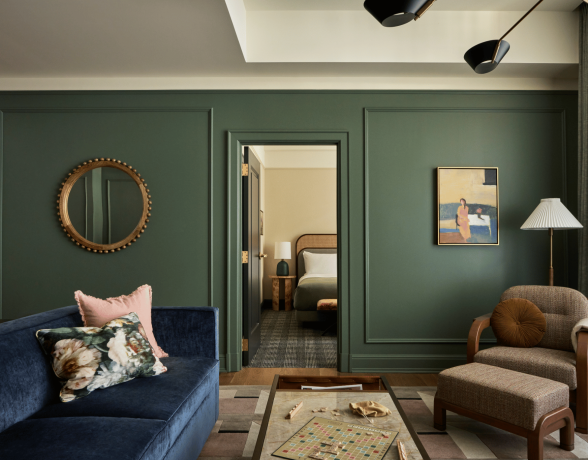 Cincinnati's Fidelity Hotel's Alfred Suite. Couch with floral pillows on left, lounge chair on right and hotel bed peeking through open doorway.