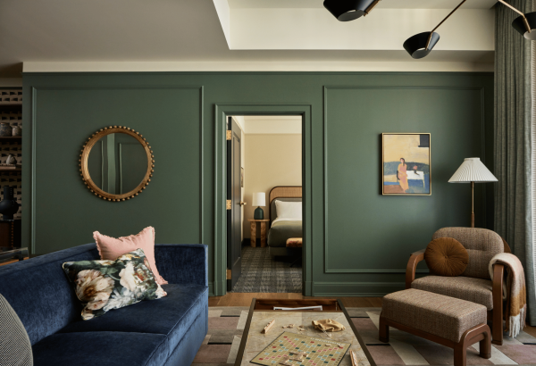 Cincinnati's Fidelity Hotel's Alfred Suite. Couch with floral pillows on left, lounge chair on right and hotel bed peeking through open doorway.